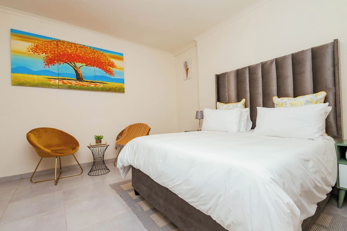 Un dormitorio con una cama grande, un cuadro de un árbol, una silla y una mesita.