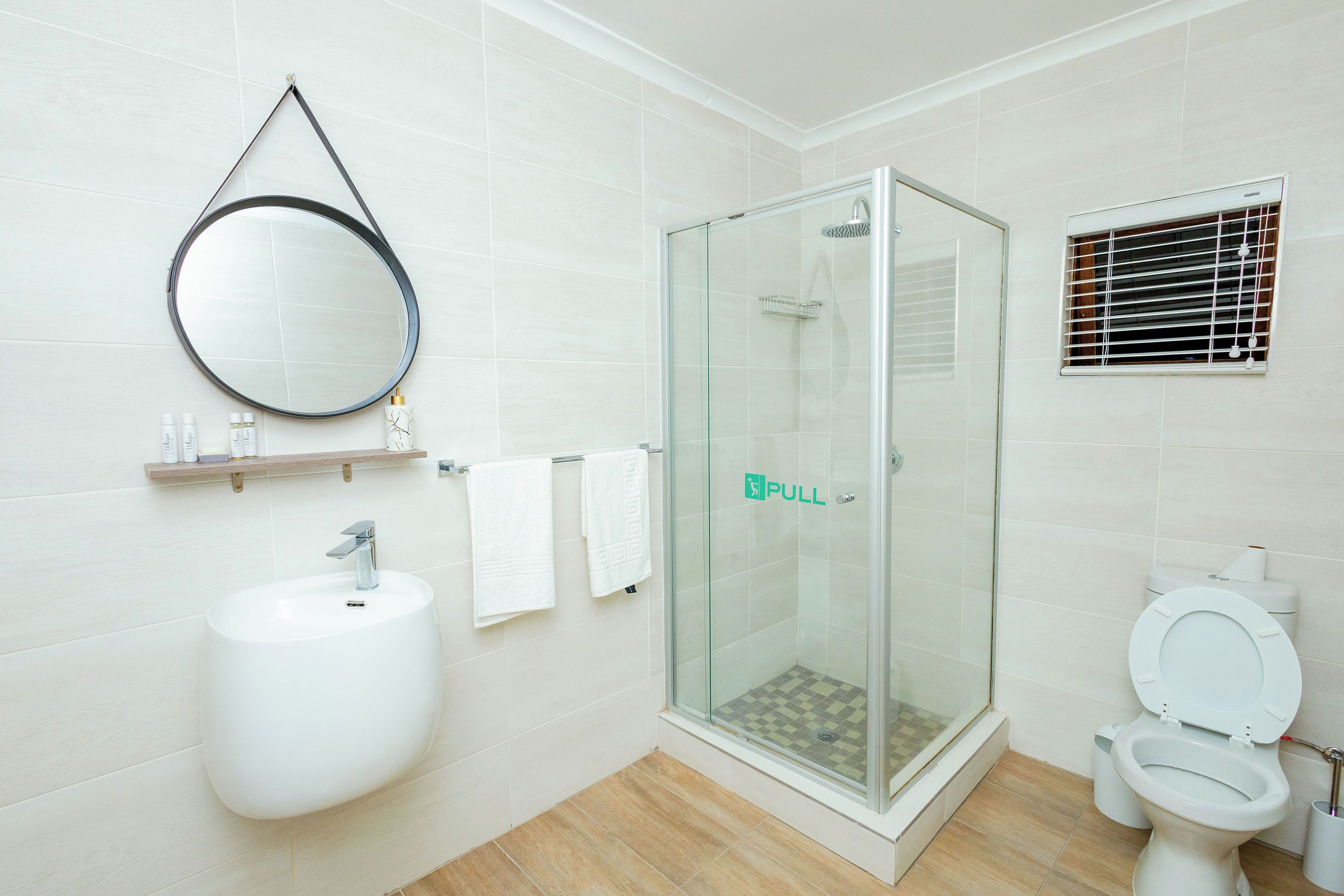 Et moderne badeværelse med et brusebad bag glas, en hvid vask og et toilet.