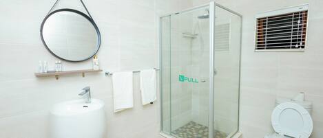 Et moderne badeværelse med et brusebad bag glas, en hvid vask og et toilet.