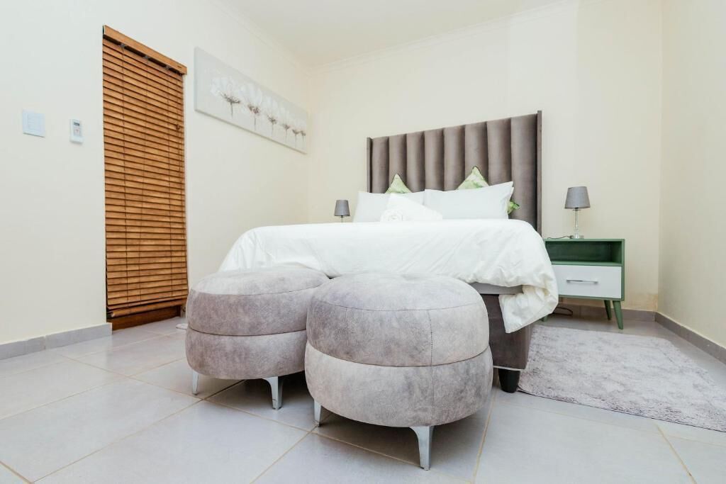 A bedroom with a bed, two bedside tables, a wall-mounted artwork, a wooden door, and a floor lamp.