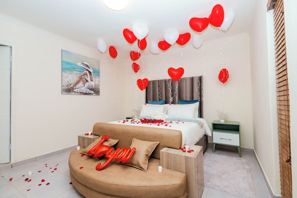 Un dormitorio con cama, mesita de noche, sofá y globos con forma de corazón.