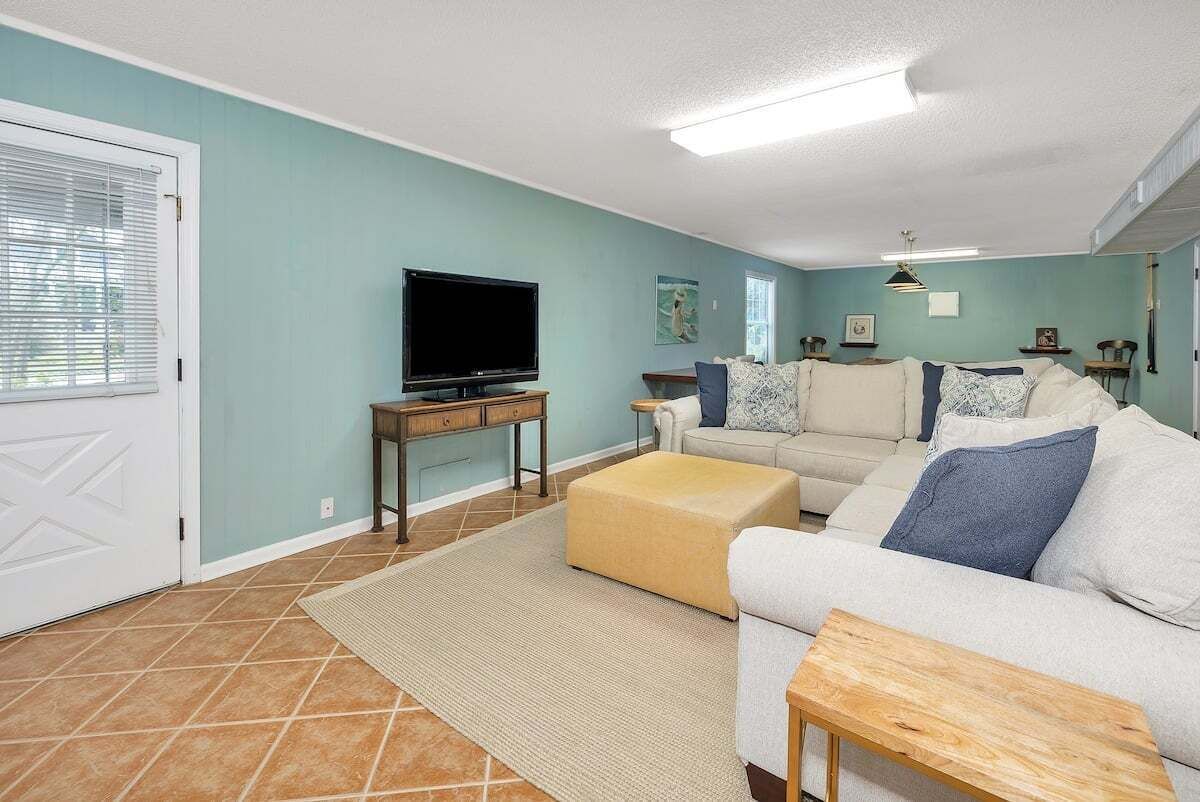 Ein Wohnzimmer mit einer Couch, einem Hocker und einem Fernseher auf einem Schrank.