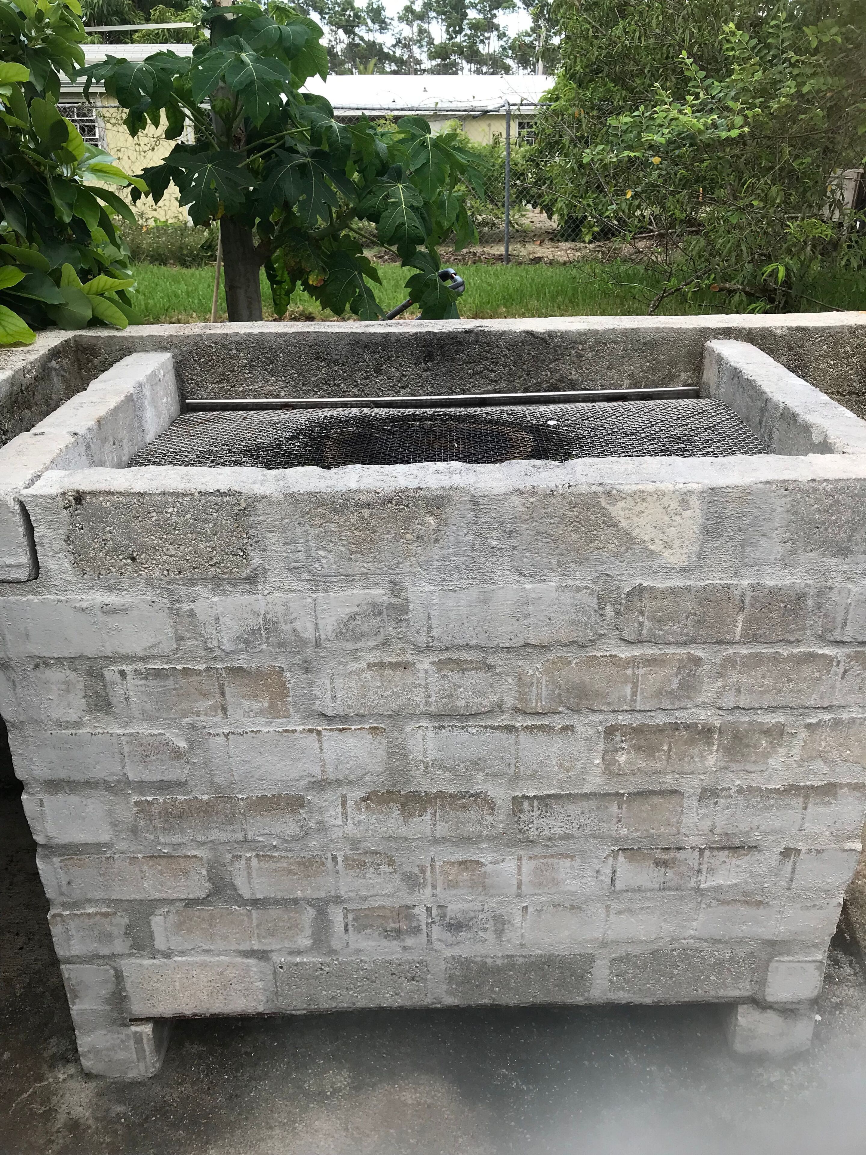 A concrete planter with a metal mesh bottom, surrounded by greenery.
