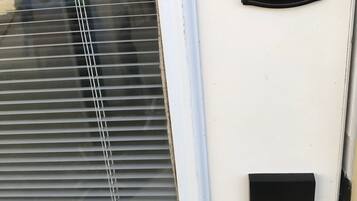 A door with a keypad lock, a window with blinds, and a small black panel below the lock.