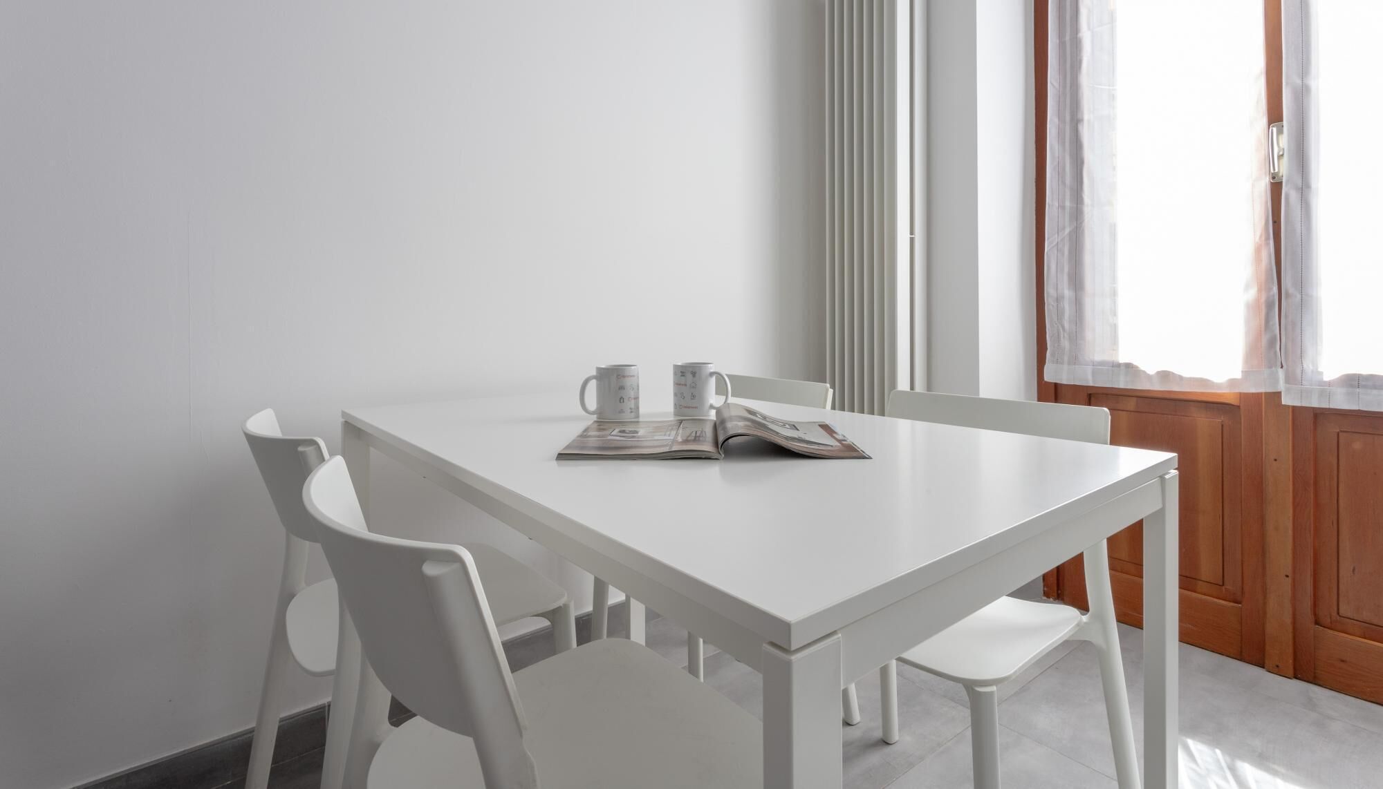 A white dining table with two chairs, a magazine, and two mugs.