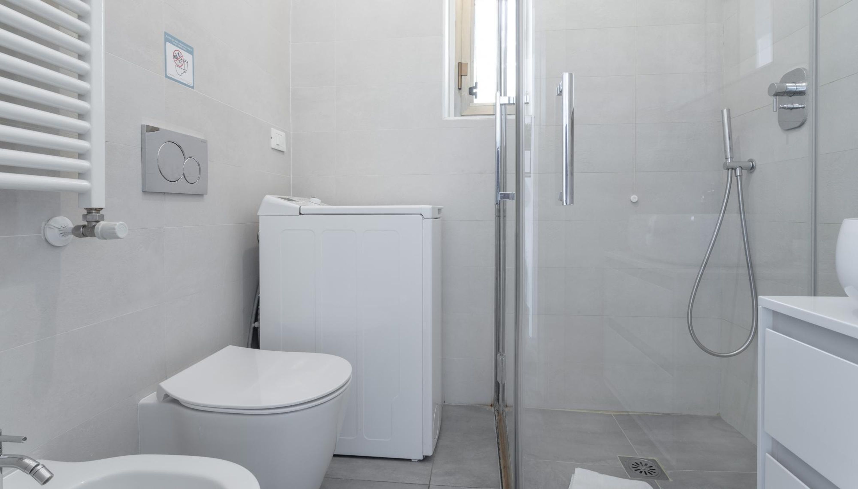 A modern bathroom with a toilet, a washing machine, a shower, and a sink.