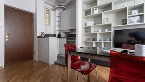 A modern kitchen with a built-in oven, a dining table with chairs, and a bookshelf filled with books and decorative items. - Italianway Easy - Abruzzi 19 (Milan)