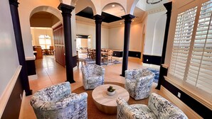 Un hall d’entrée spacieux, doté de hauts plafonds, de colonnes sombres et d’un espace salon central agrémenté de fauteuils à motifs et d’une table basse ronde.