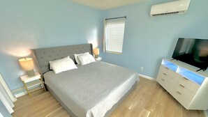 Een slaapkamer met een bed, nachtkastjes, een televisie en een airconditioner.