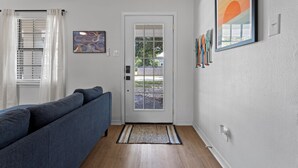 Un pasillo con un sofá azul, una puerta blanca con paneles de vidrio y una alfombra estampada.