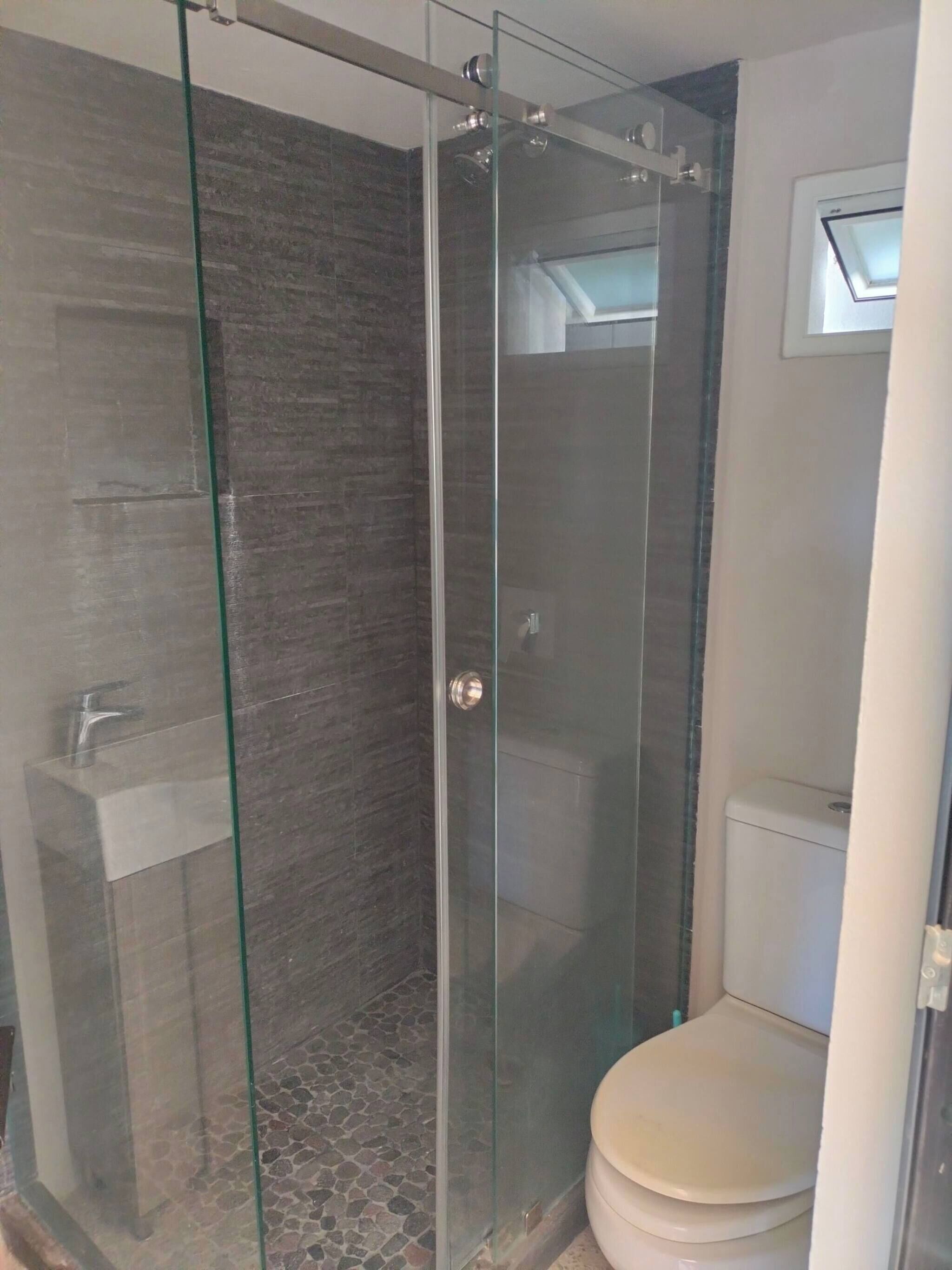 Un baño con ducha separada por vidrio, inodoro y lavamanos.