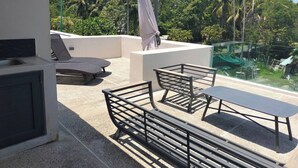 Een balkon met een tafel en stoelen, een hangstoel en uitzicht op palmbomen en groen.
