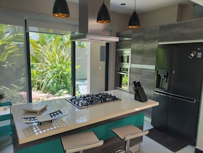 A modern kitchen with a central island, stainless steel appliances, and a view of greenery outside.