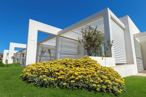 A modern building with white structural elements and a garden with yellow flowers.