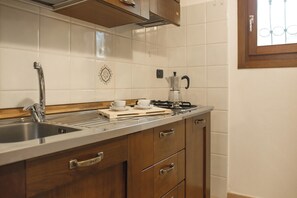 Een keuken met een roestvrijstalen spoelbak, houten kastjes, een koffiezetapparaat en een raam met metalen tralies.