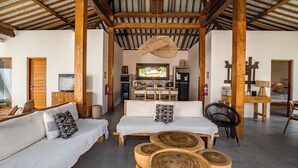 A spacious living area with a high ceiling, wooden beams, a sofa set, a dining table, and a television. - Villa Parasol by Alfred in Bali (Seminyak)