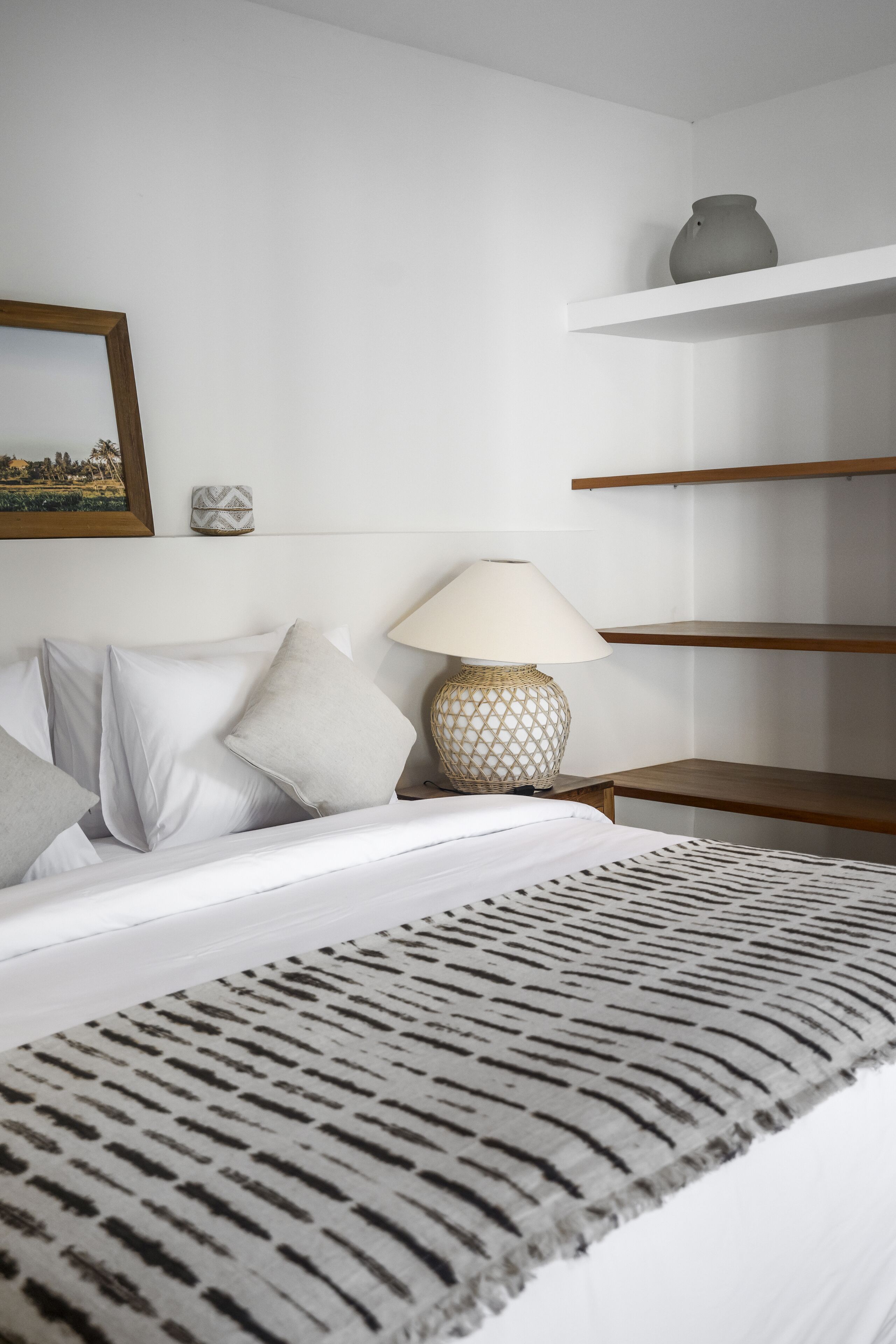 A neatly arranged bedroom with a bed, pillows, a lamp, and shelves.