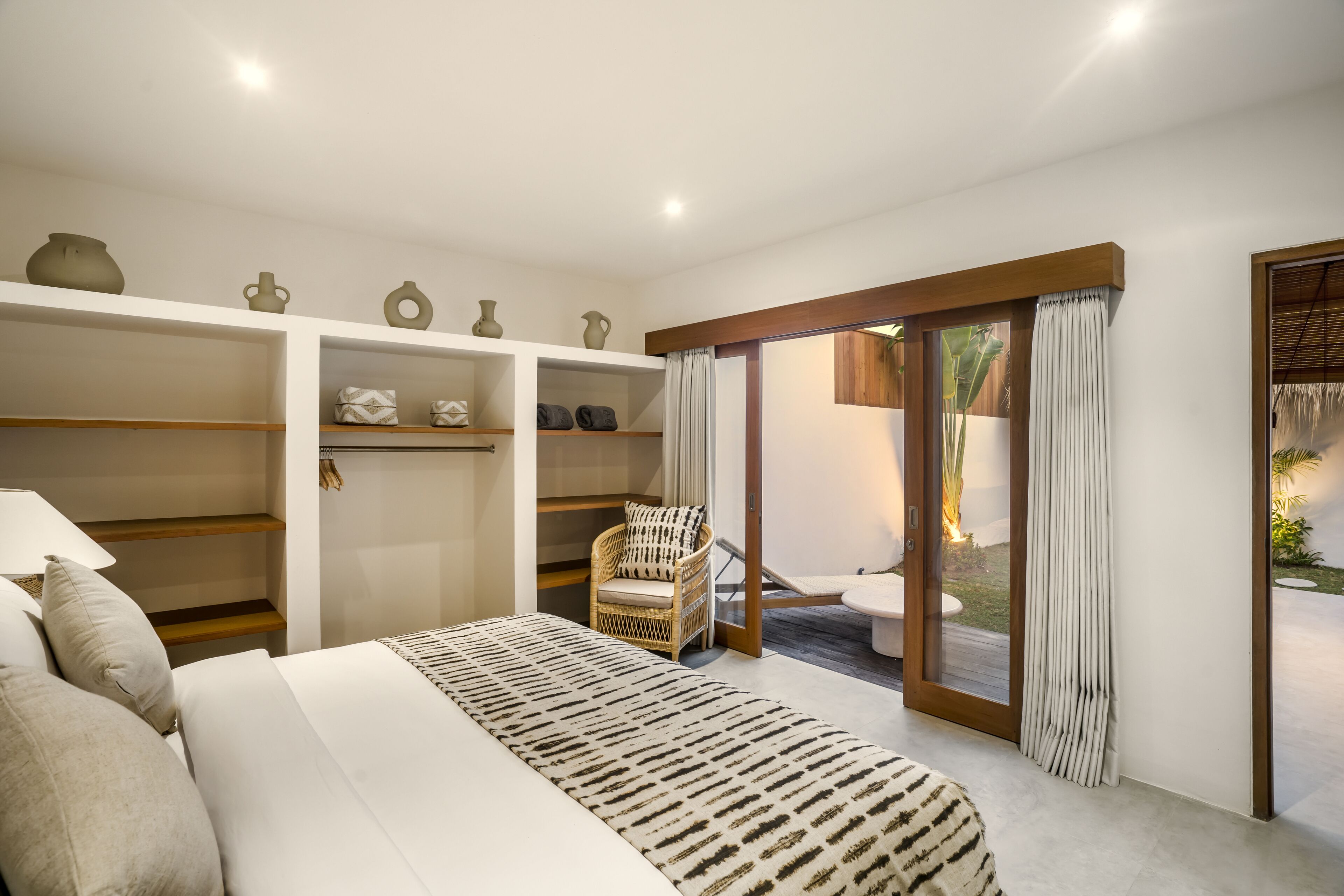 A bedroom with a bed, a chair, a wardrobe, and a sliding glass door leading to an outdoor area.