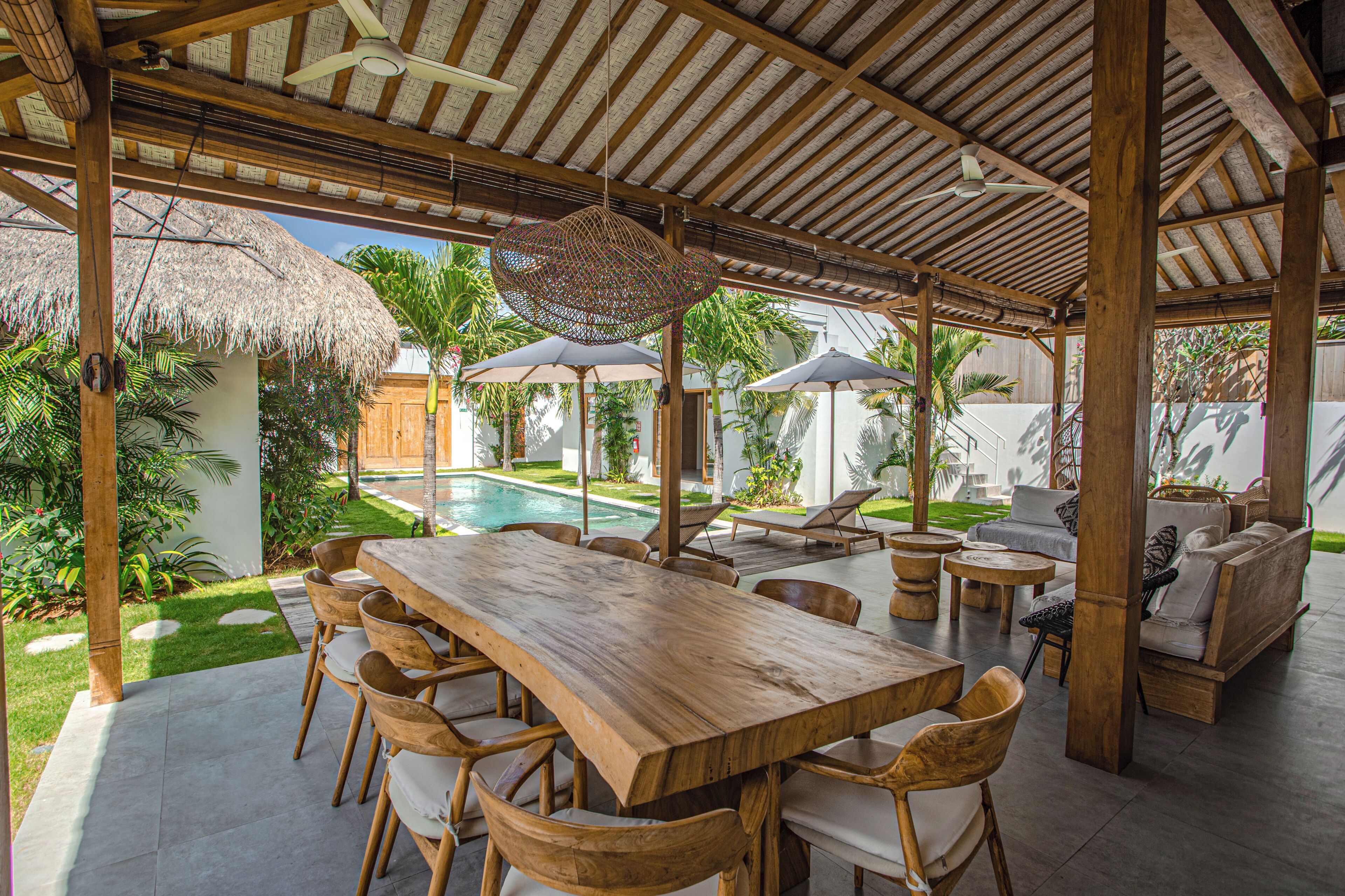 An outdoor patio with a wooden table and chairs, a pool, and lounge areas.
