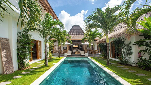 A swimming pool with a thatched-roof building in the background, surrounded by palm trees and a well-maintained lawn. - Villa Parasol by Alfred in Bali (Seminyak)
