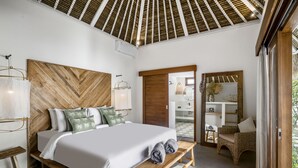 A bedroom with a wooden headboard, a bed with white linens, a bench with towels, and a wicker chair. - Villa Parasol by Alfred in Bali (Seminyak)