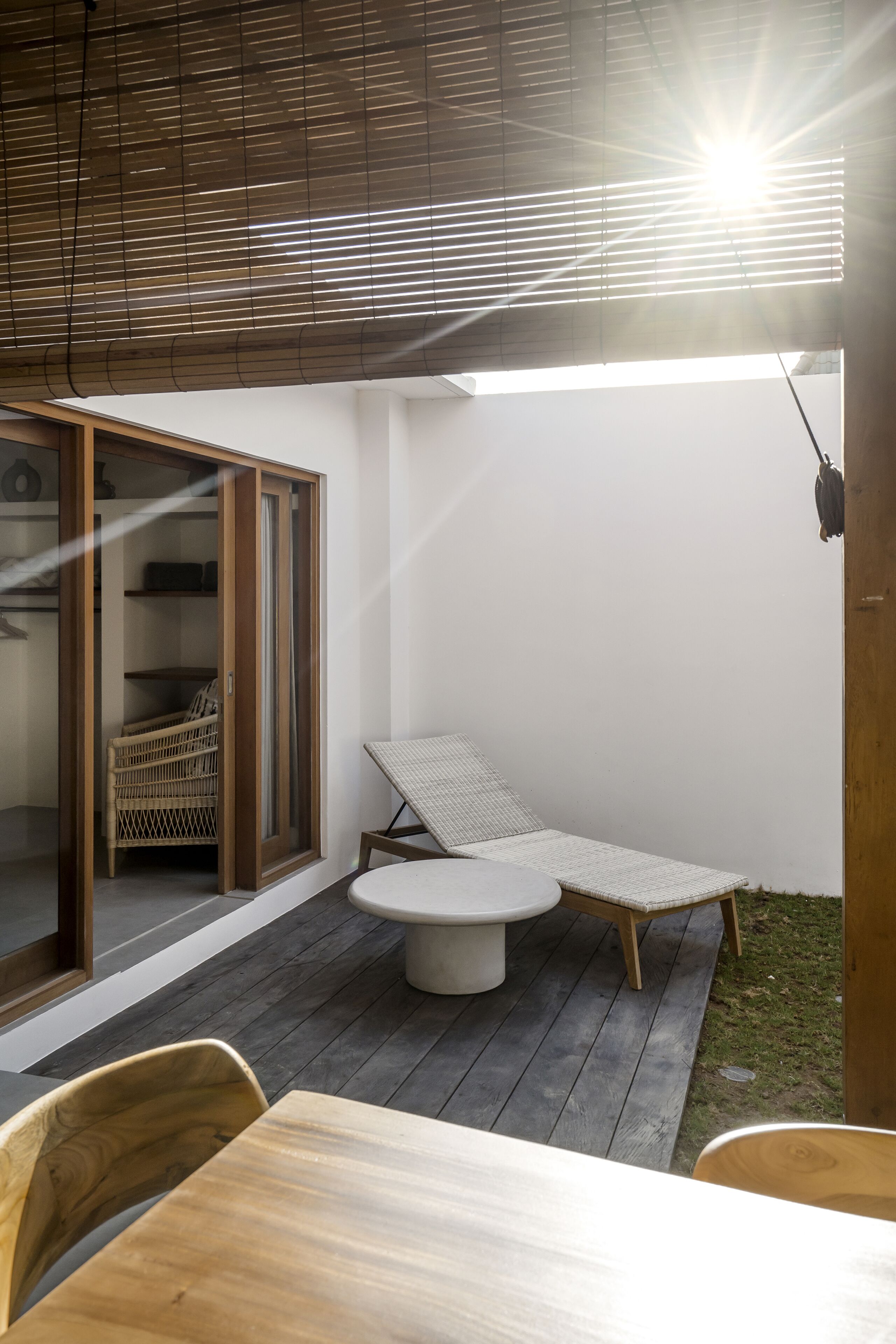 A patio area with a table and chairs, a cushioned lounge chair, and a wicker basket in a wooden-framed sliding door.