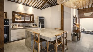 A modern kitchen with a large island, wooden chairs, and a hanging light fixture. - Villa Parasol by Alfred in Bali (Seminyak)