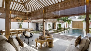 A covered outdoor area with a pool, wooden furniture, and a dining table. - Villa Parasol by Alfred in Bali (Seminyak)