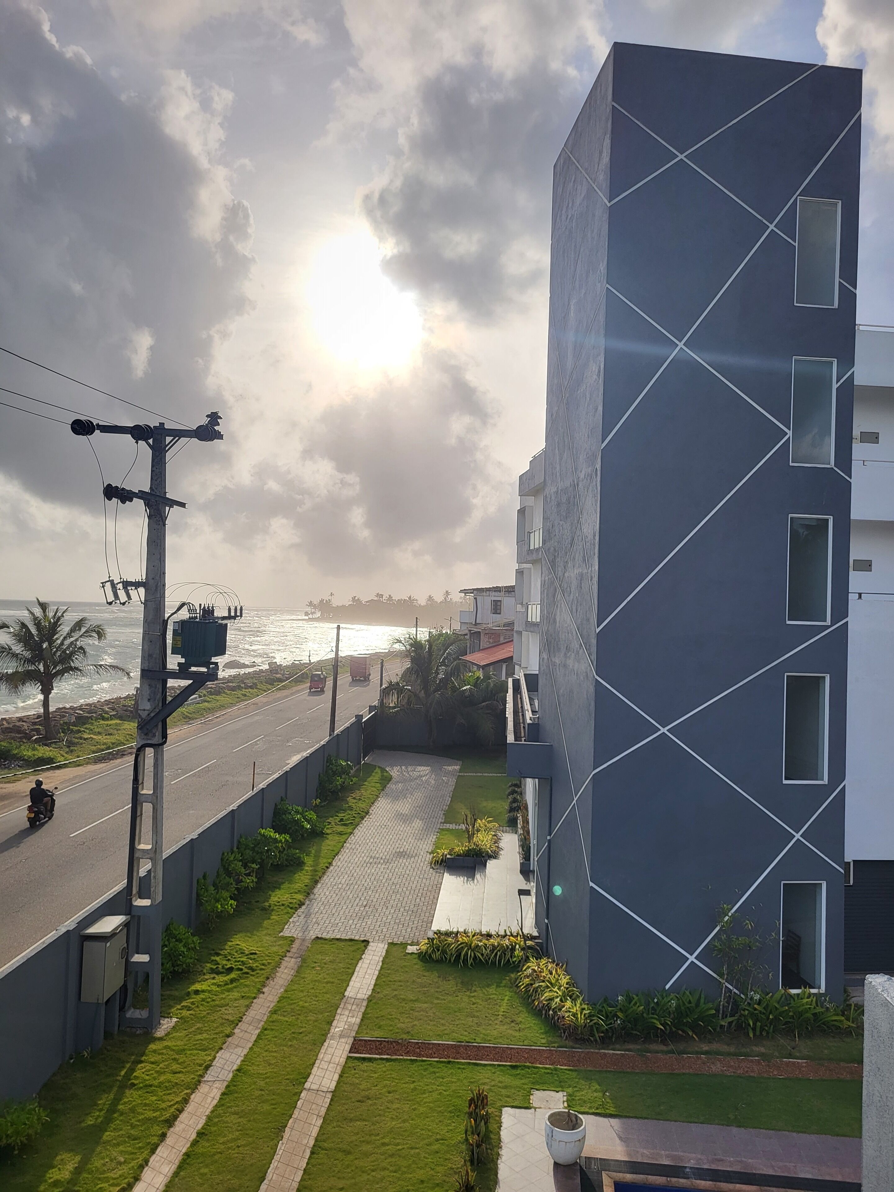 A modern building with a geometric facade, a paved pathway, and a view of the sea.