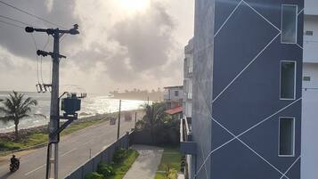 A modern building with a geometric facade, a paved pathway, and a view of the sea.