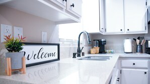 Una cocina con armarios blancos, un lavamanos de acero inoxidable y un letrero de bienvenida.