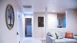 Una sala de estar moderna con un sofá gris, un espejo y una obra de arte de pared con forma de árbol decorativo.