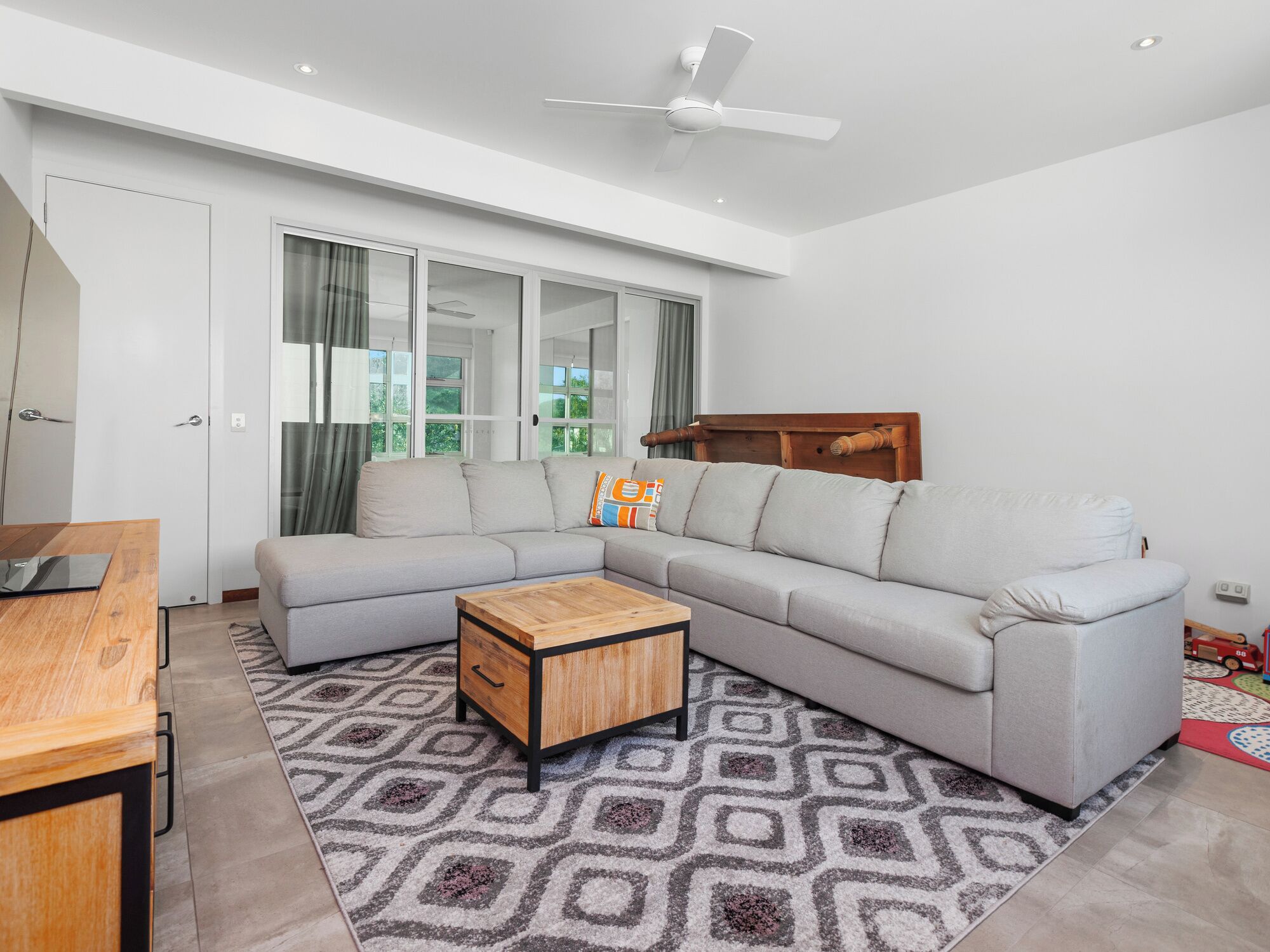 Un salón moderno con un sofá modular gris, una mesa de centro de madera y una alfombra estampada.