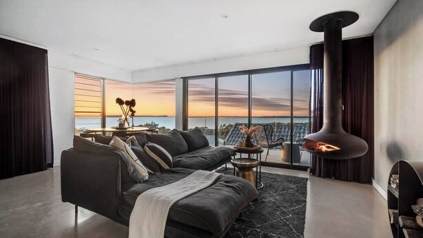 A modern living room with a large sofa, a fireplace, and a city view. - 'Cloud Nine' - Spa, Sauna, Iconic Jervis Bay Views (Vincentia)