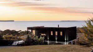 A modern building with a flat roof, surrounded by a landscaped garden with a view of the sea. - 'Cloud Nine' - Spa, Sauna, Iconic Jervis Bay Views (Vincentia)