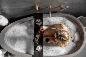 Une baignoire dans laquelle est assise une personne, une bougie et un plateau avec des biscuits.