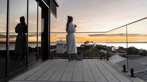 A balcony with a glass railing overlooking a sunset view. - 'Cloud Nine' - Spa, Sauna, Iconic Jervis Bay Views (Vincentia)