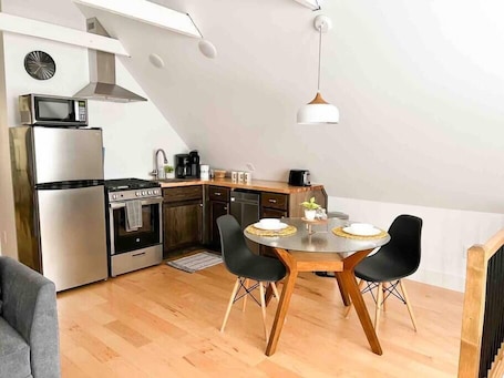 A compact kitchen with modern appliances, a dining area with a round table and chairs, and a loft-style ceiling with exposed beams.