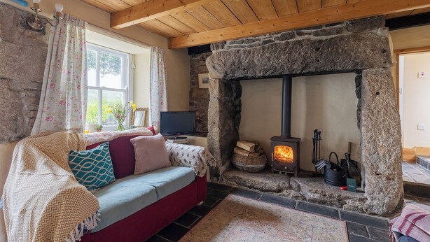 A cozy room with a stone fireplace, a wooden ceiling, and a red sofa with patterned cushions.