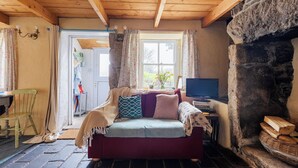 A cozy room with a wooden ceiling, a stone fireplace, a sofa with cushions, a television, and a window with curtains.
