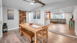 A spacious living area with a wooden dining table, a sofa, and a ceiling fan. - Quiet Neighborhood! Close to Beach. Private Backyard w/ Gas Grill ~ Turtle Crossing (Largo)