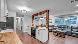 A modern kitchen with a wooden island, a dining area with a wooden table, and a living room with a leather couch and a large window. - Quiet Neighborhood! Close to Beach. Private Backyard w/ Gas Grill ~ Turtle Crossing (Largo)