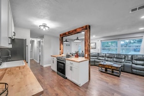 Eine moderne Küche mit einer zentralen Kochinsel, ein Essbereich mit einem Holztisch und ein Wohnzimmer mit einer Ledersofa.
