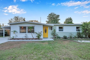 A single-story house with a yellow front door, a small porch, and a well-maintained lawn.