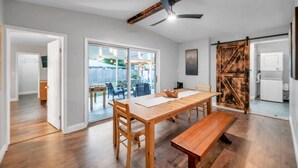 A spacious dining area with a wooden table and benches, a ceiling fan, and a sliding barn-style door. - Quiet Neighborhood! Close to Beach. Private Backyard w/ Gas Grill ~ Turtle Crossing (Largo)