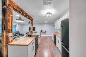 A modern kitchen with a wooden countertop, white cabinets, and a large black refrigerator. There is a dining area with a table and chairs, and a kitchen island with a sink and countertop.