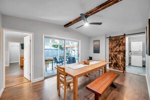 A spacious dining area with a wooden table and benches, a ceiling fan, and a sliding barn-style door.