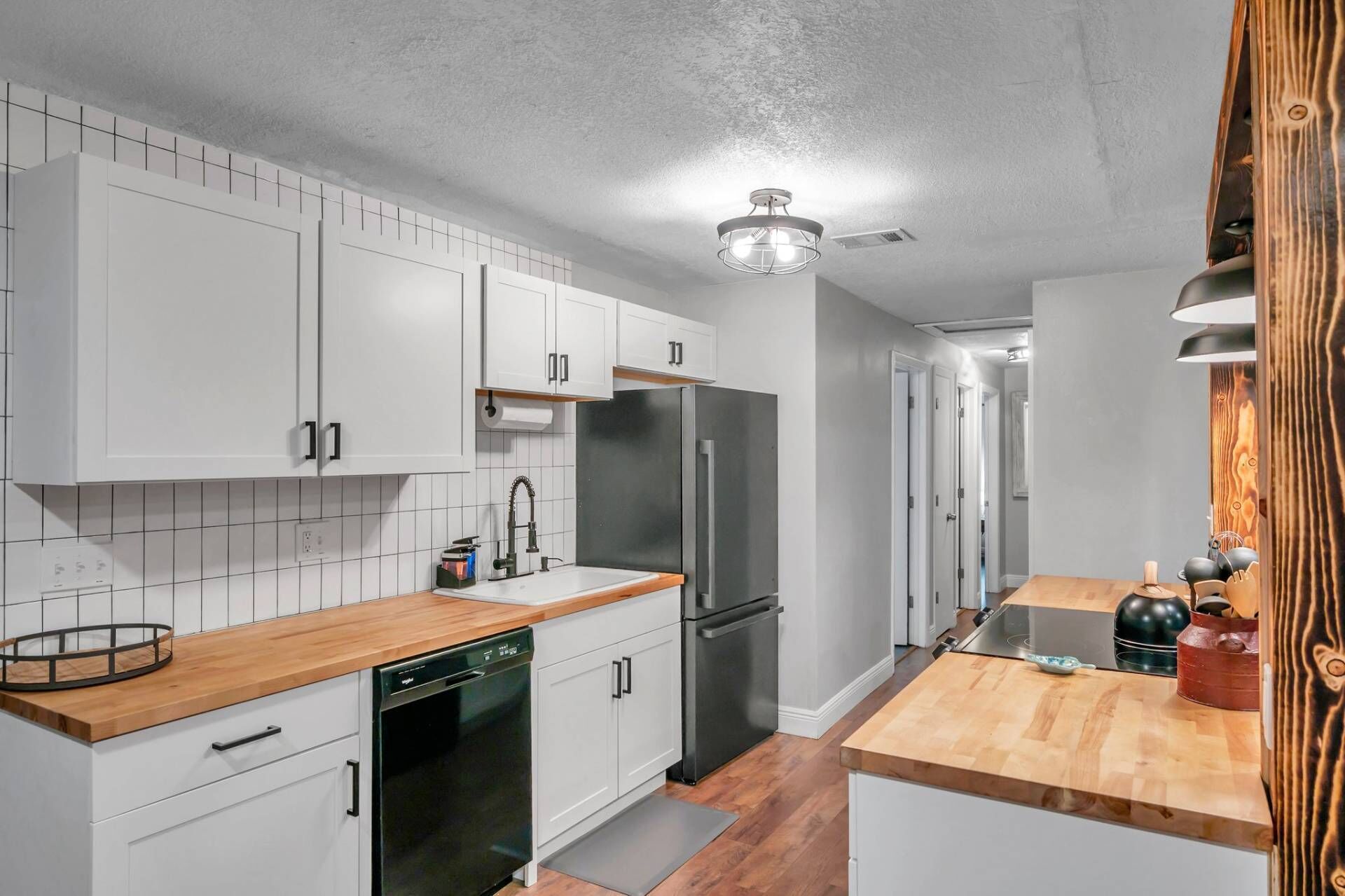 Une cuisine moderne avec des meubles blancs, un réfrigérateur en acier inoxydable et des plans de travail en bois.
