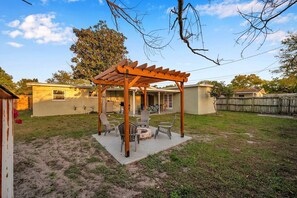 Un jardin avec une pergola en bois, un espace salon extérieur et un foyer.
