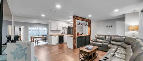 Una sala moderna con un sofá de cuero, una mesa de centro de madera y una cocina al fondo.